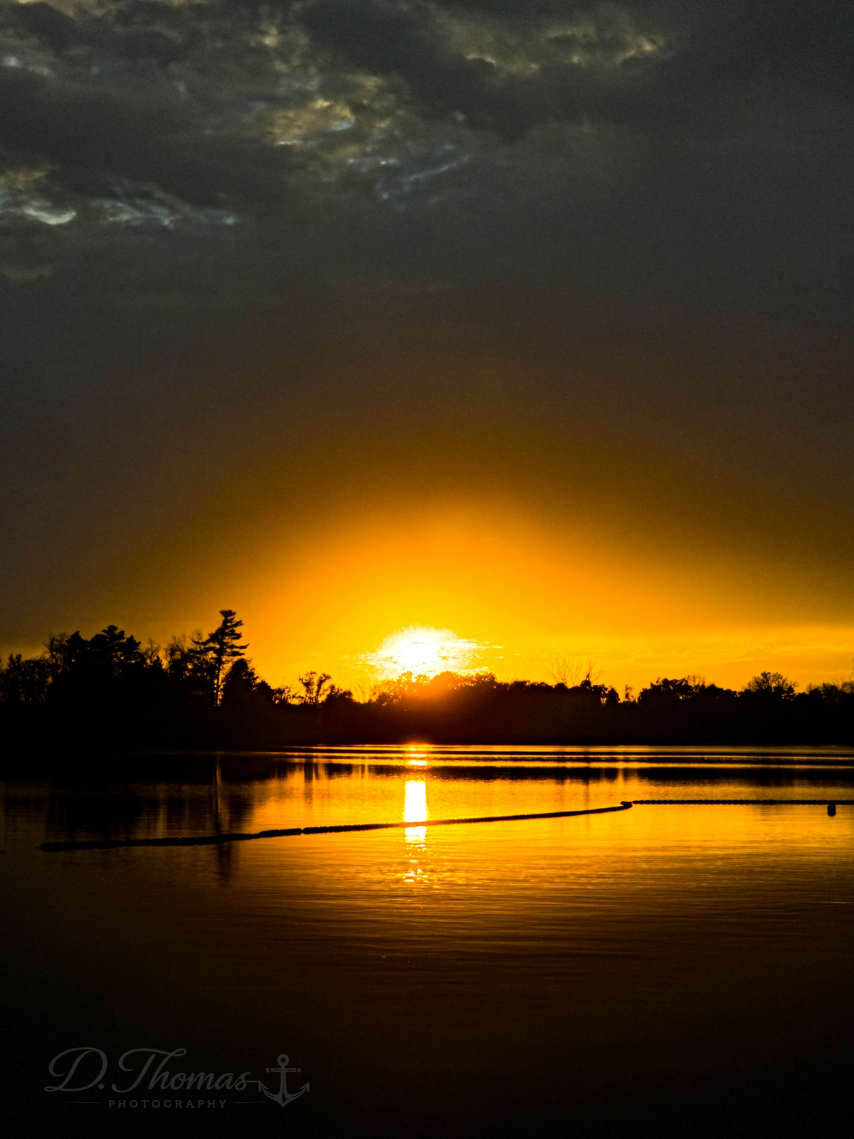 Brilliant orange sunset glowing over a calm lake with dark tree silhouettes